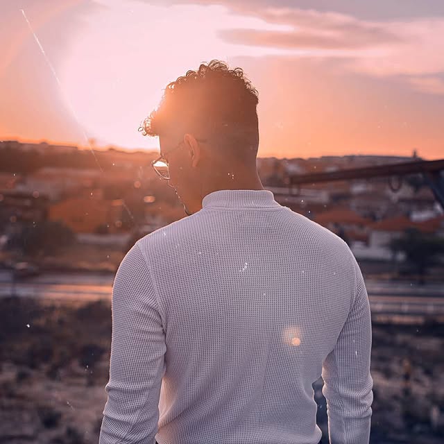 Persona observando el atardecer con una vista de fondo desde una colina.