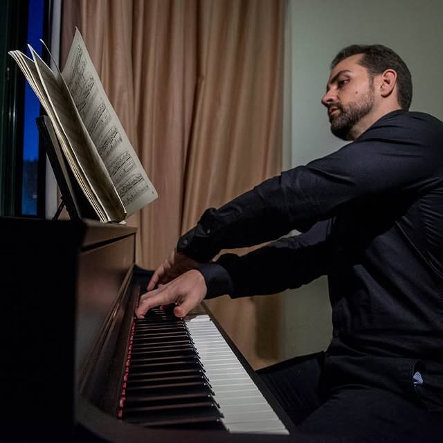 Hombre tocando el piano mientras lee una partitura en un espacio profesional.
