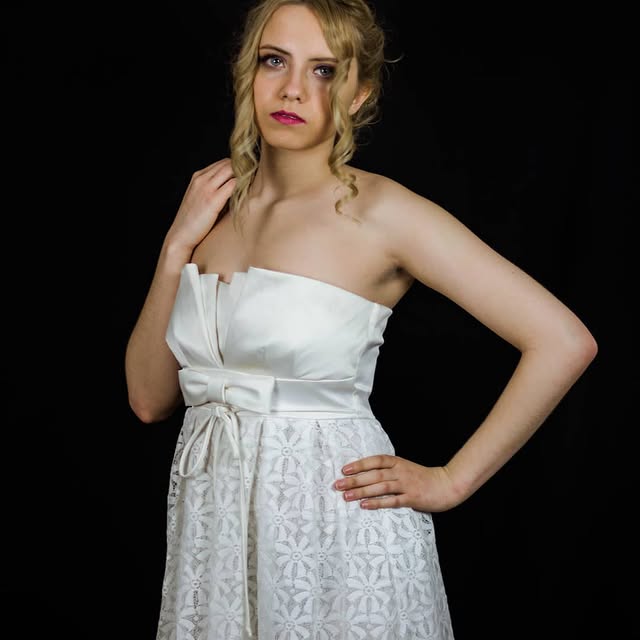 Modelo con vestido blanco posando en un fondo negro durante una sesión fotográfica.