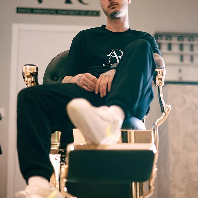 Hombre sentado en una silla dorada posando para una sesión fotográfica.