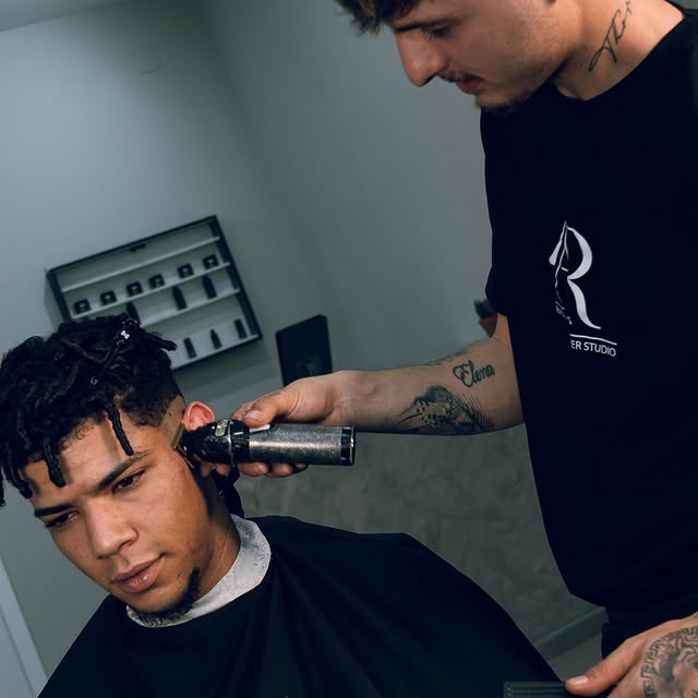Barbero trabajando en un corte de cabello detallado en una barbería.