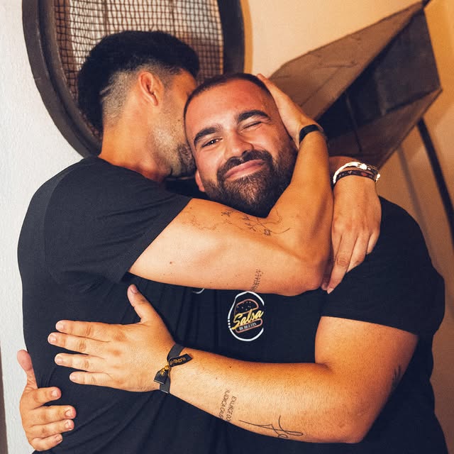 Dos hombres abrazándose y sonriendo en un ambiente relajado.