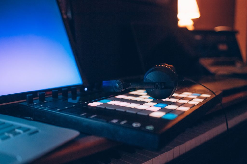 Mesa de producción musical con controladores, auriculares y portátil iluminados en estudio profesional.